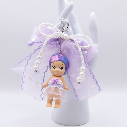 Silver heart keychain featuring Sonny Angel HYDRANGEA figure from the Flower series with a purple sequined bow and faux pearls on a white background