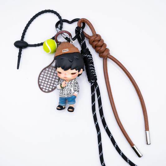 Black heart keychain with Hirono Alienegra figure from POP MART's Clot series and matching charms including brown faux leather lanyard, black lanyard, rubber chain, brown racket, and yellow tennis ball.