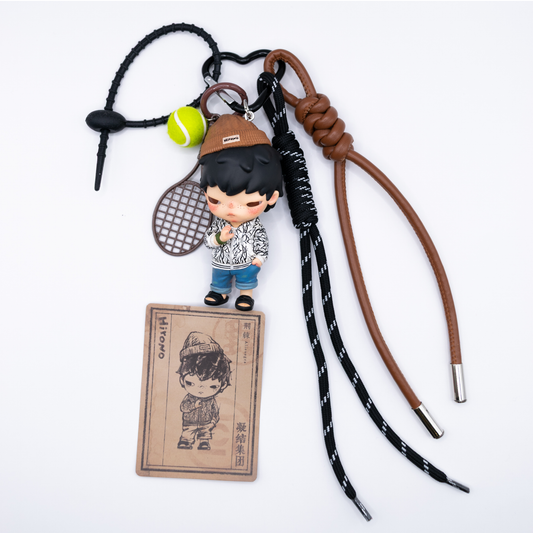 Black heart keychain with Hirono Alienegra figure from POP MART's Clot series and matching charms including brown faux leather lanyard, black lanyard, rubber chain, brown racket, and yellow tennis ball next to its card.
