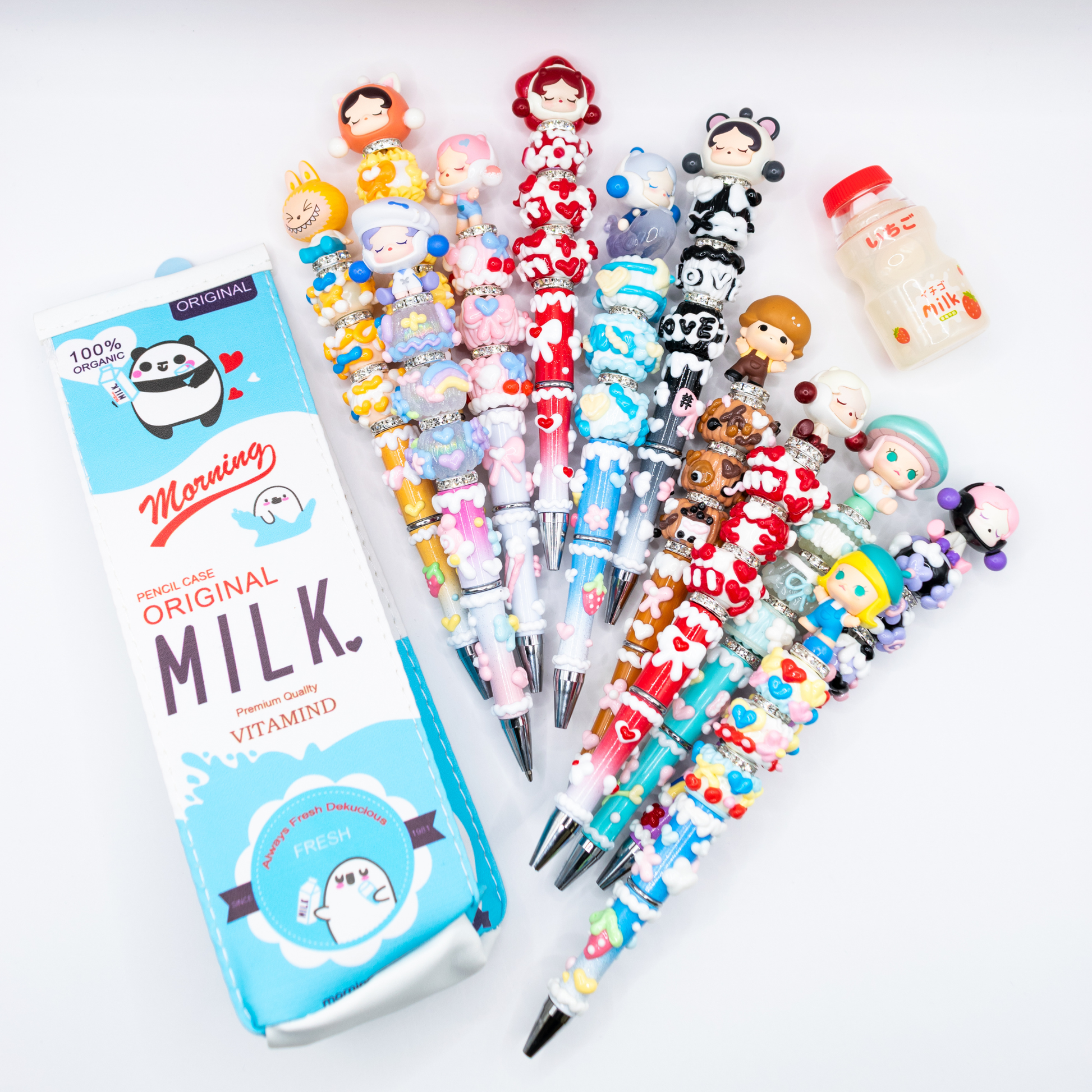 Collection of colorful beaded pens pens with pop beans  on a white background, next to a pencil case shaped as a milk carton and a pen eraser shaped as a milk bottle.