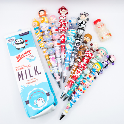 Collection of colorful beaded pens pens with pop beans  on a white background, next to a pencil case shaped as a milk carton and a pen eraser shaped as a milk bottle.