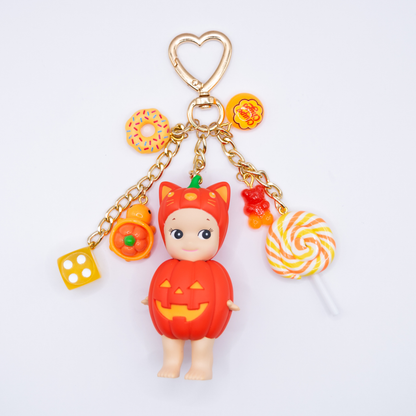 Orange Sonny Angel CAT from Pumpkin Patch Series with donut, chupa chups, dice, turtle gummy bear and lollipop charms in matching colors on a golden heart keychain