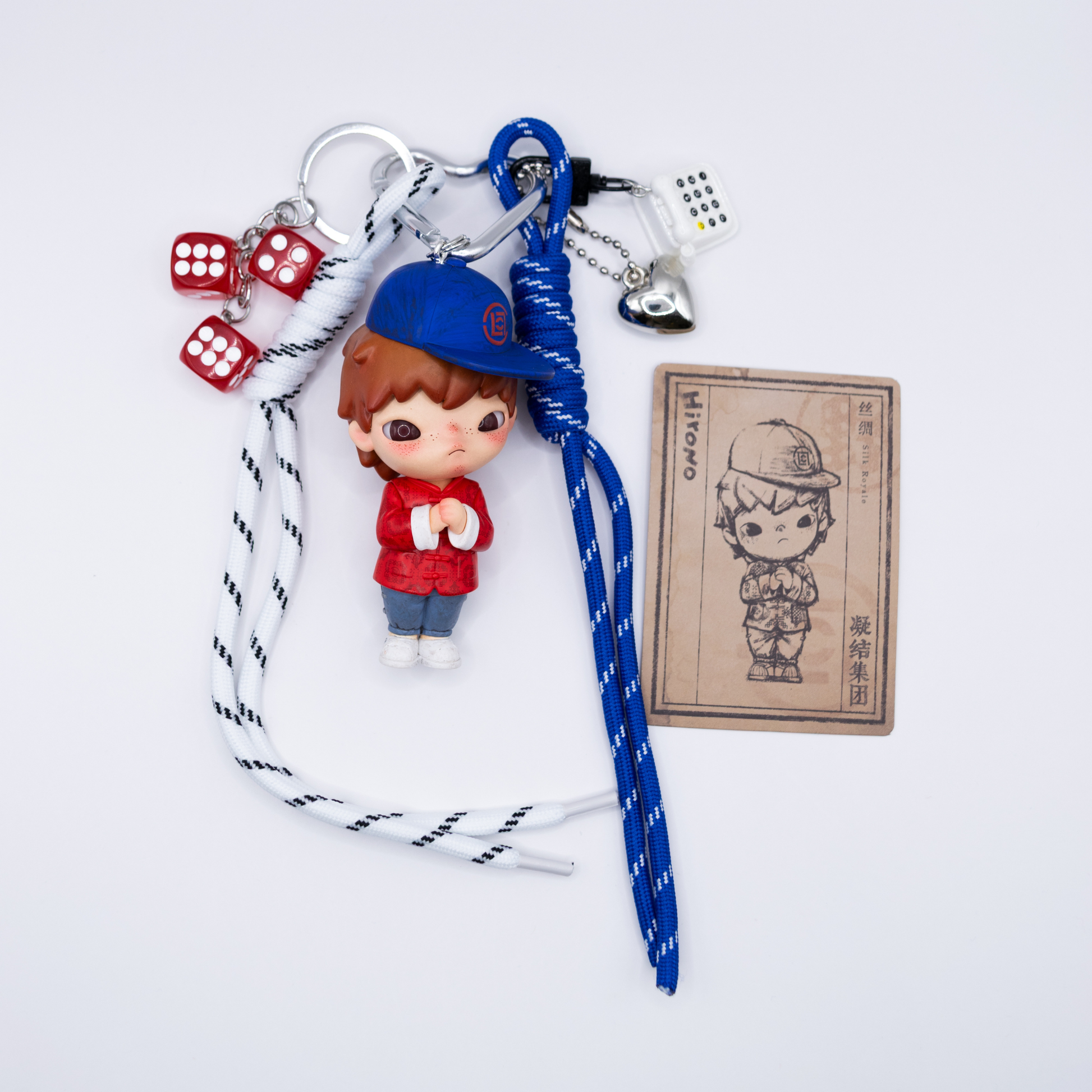Silver heart keychain with Hirono Silk Royale figure from POP MART's Clot series and matching charms including blue lanyard, black and white lanyard, silver heart, white rotary phone, three red dice next to its card.