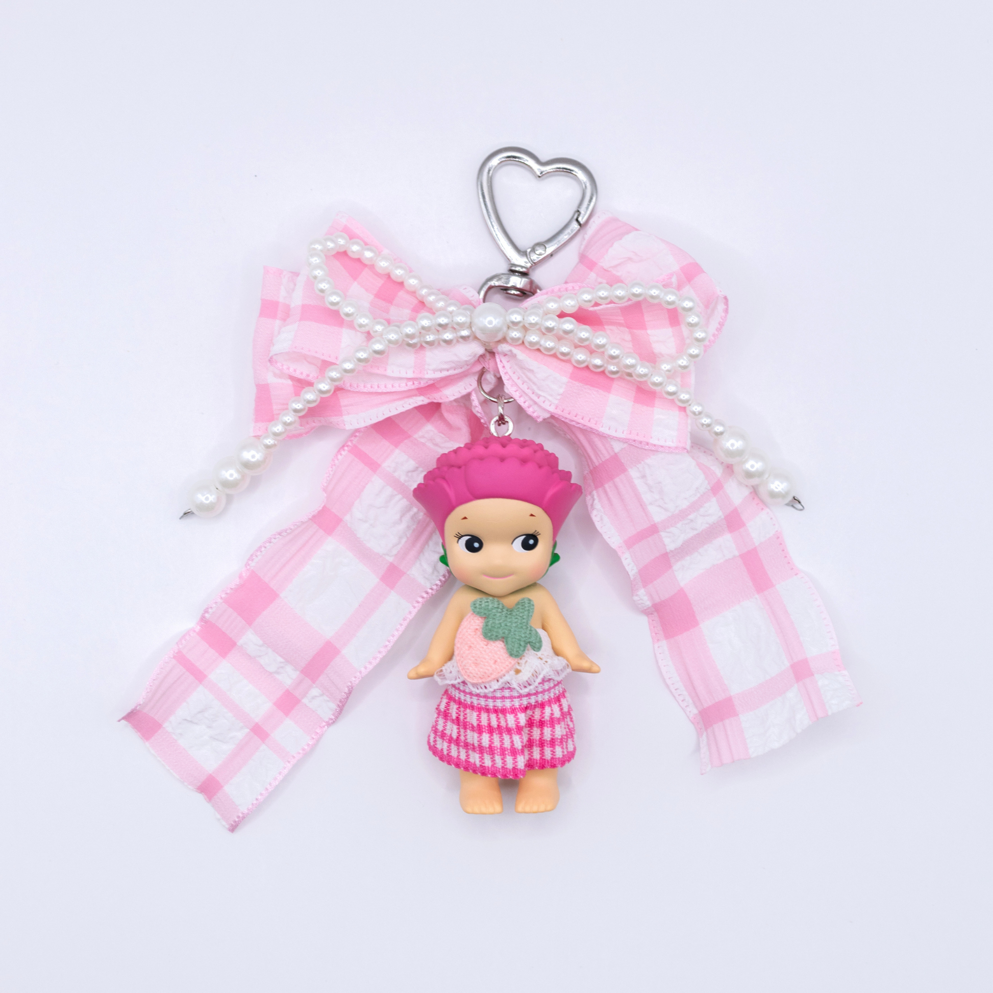 Silver heart keychain featuring Sonny Angel Carnation figure with a pink gingham bow and faux pearls on a white background
