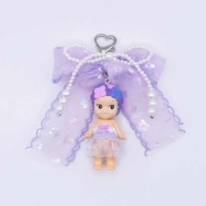 Silver heart keychain featuring Sonny Angel HYDRANGEA figure from the Flower series with a purple sequined bow and faux pearls on a white background