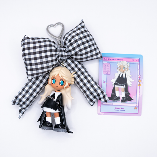 Silver keychain with Lil Peach Riot  Poppy Saint from POP MART's Loading series on a black and white gingham bow next to its card
