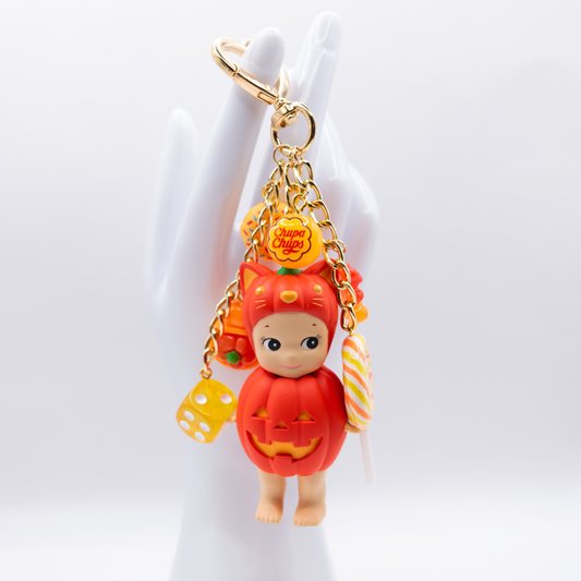Orange Sonny Angel CAT from Pumpkin Patch Series with donut, chupa chups, dice, turtle gummy bear and lollipop charms in matching colors on a golden heart keychain