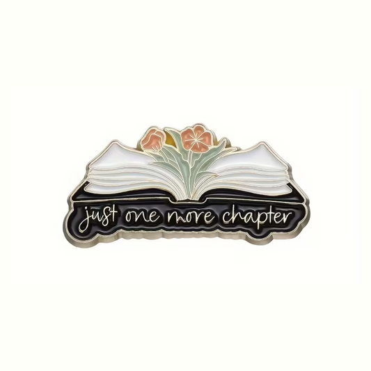 Enamel pin with an open book design and 'just one more chapter' text on a white background