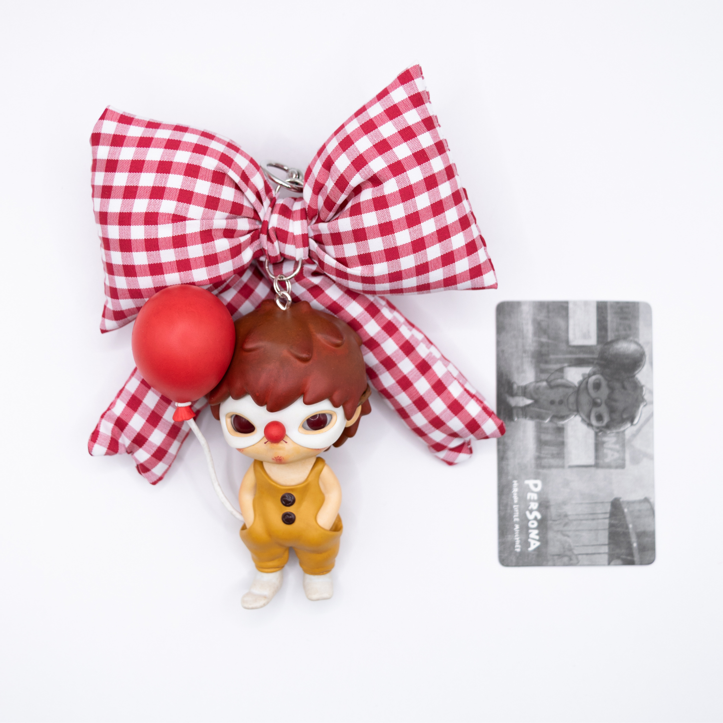 Silver keychain with red and white checkered bow and Hirono Persona figure from POP MART's Little Mischief series next to its card.