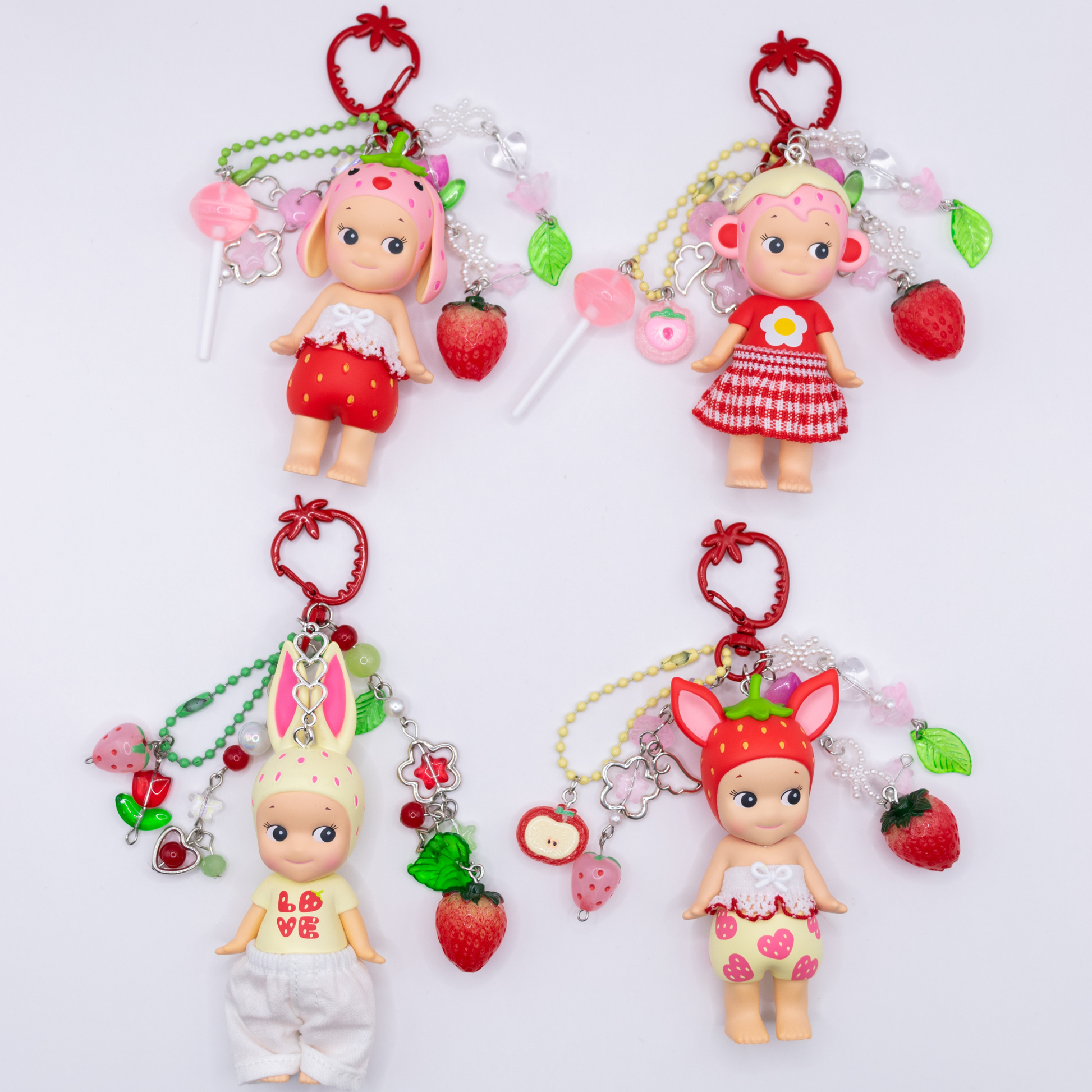 Four Sonny Angel keychains with figures from the Strawberry Love series on a red strawberry clasps with matching beads