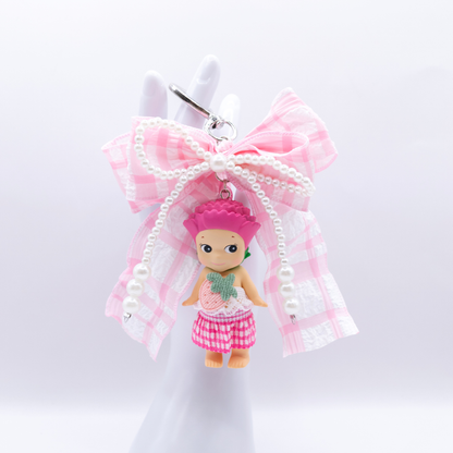 Silver heart keychain featuring Sonny Angel Carnation figure with a pink gingham bow and faux pearls on a white background