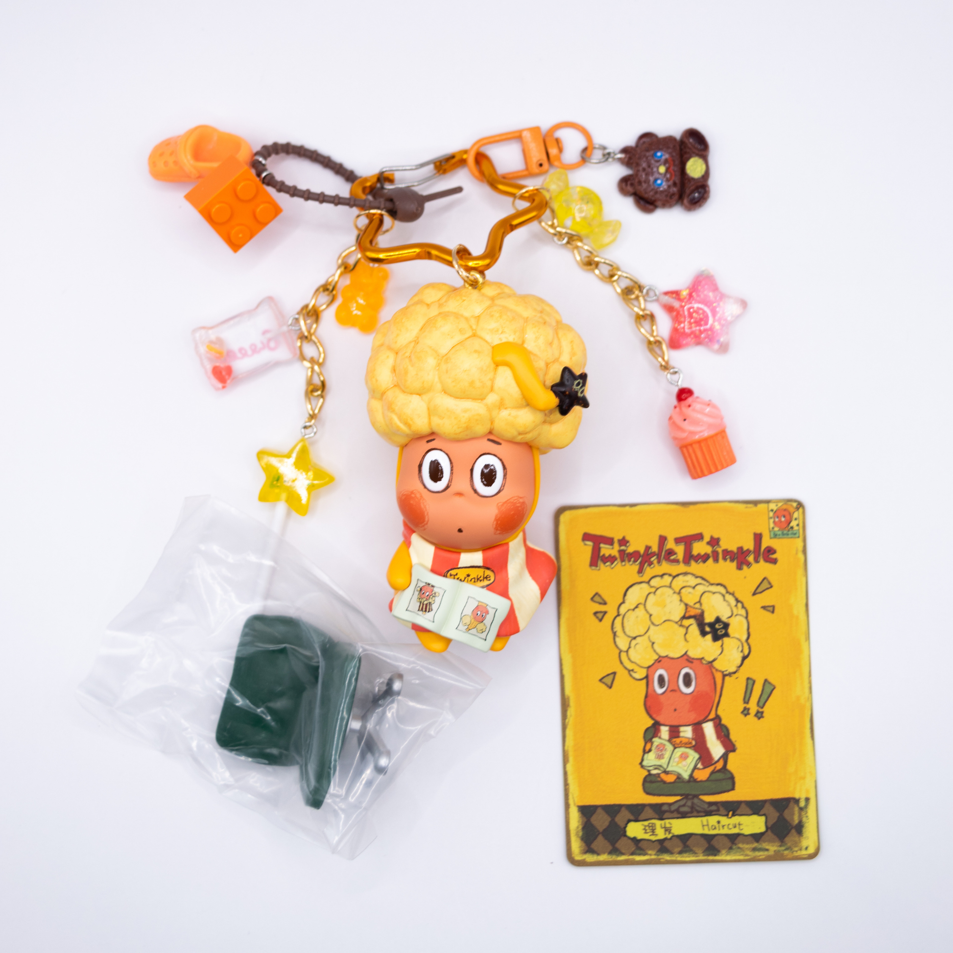 Star keychain with Twinkle Twinkle HAIRCUT figure from the Be A Little Star Series with matching orange-tones charms including star lollipop, muffin, stars, candy, lego piece, croc.