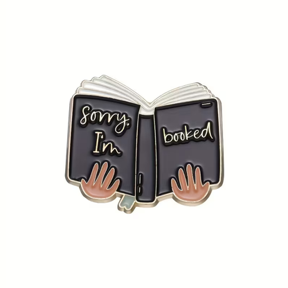 Enamel pin with an open book design and 'Sorry I'm booked' text on a white background