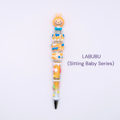 Colorful beaded pen with cartoon character design on a white background, labeled 'LABUBU Sitting Baby Series'.